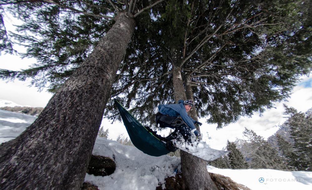 Snowboarder passing over a hammock stretched between fir trees in a snowy forest