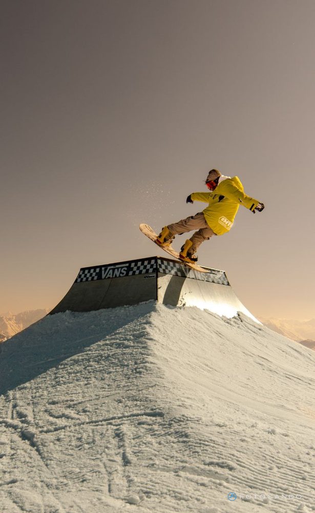 Snowboarder on the box in the Laax snowpark, in warm sunset light