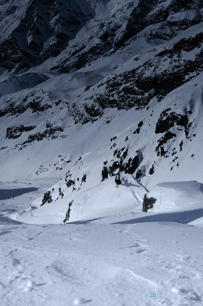 Rider freeriding down a snowy slope beneath rock walls