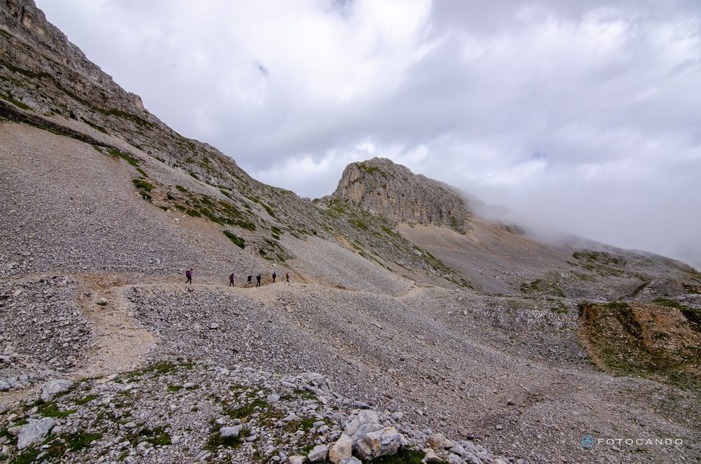 Hikers on the scree slope beneath the rock walls, July 2021